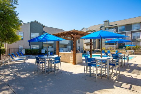 A poolside area with blue umbrellas and chairs.
