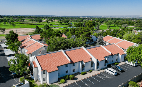 A parking lot is in front of a white building with red roofs.
