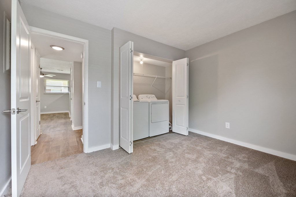 A white refrigerator is in the corner of a room with a carpeted floor.