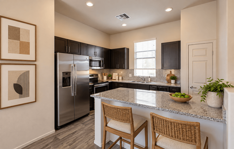 A kitchen with a refrigerator, sink, and two chairs.