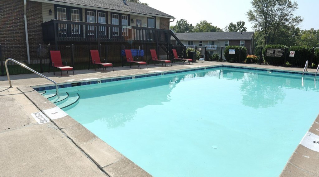 A swimming pool with red chairs and a building in the background.