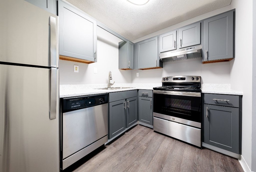 A kitchen with a refrigerator on the left and a stove top oven on the right.