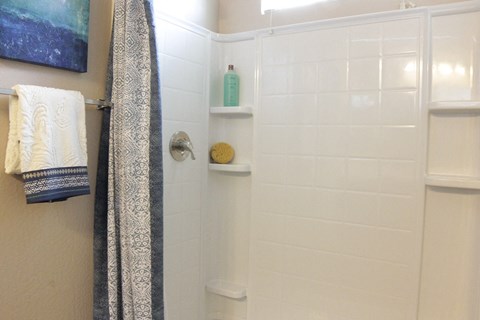 A bathroom with a white tiled shower and a white towel hanging on the wall.