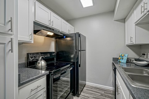 A black refrigerator is in a kitchen with white cabinets.