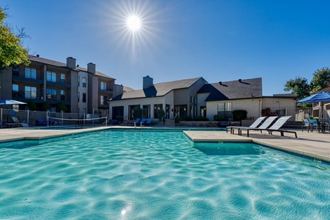 A large swimming pool in front of a building with sunlight shining.