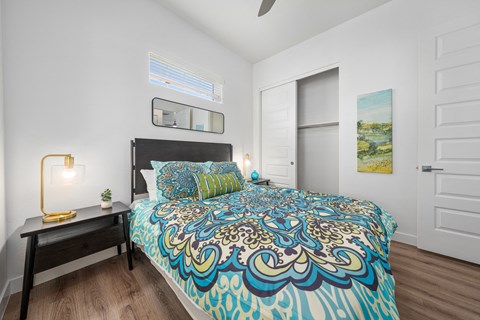 A bedroom with a bed, a nightstand with a lamp, and a painting on the wall.