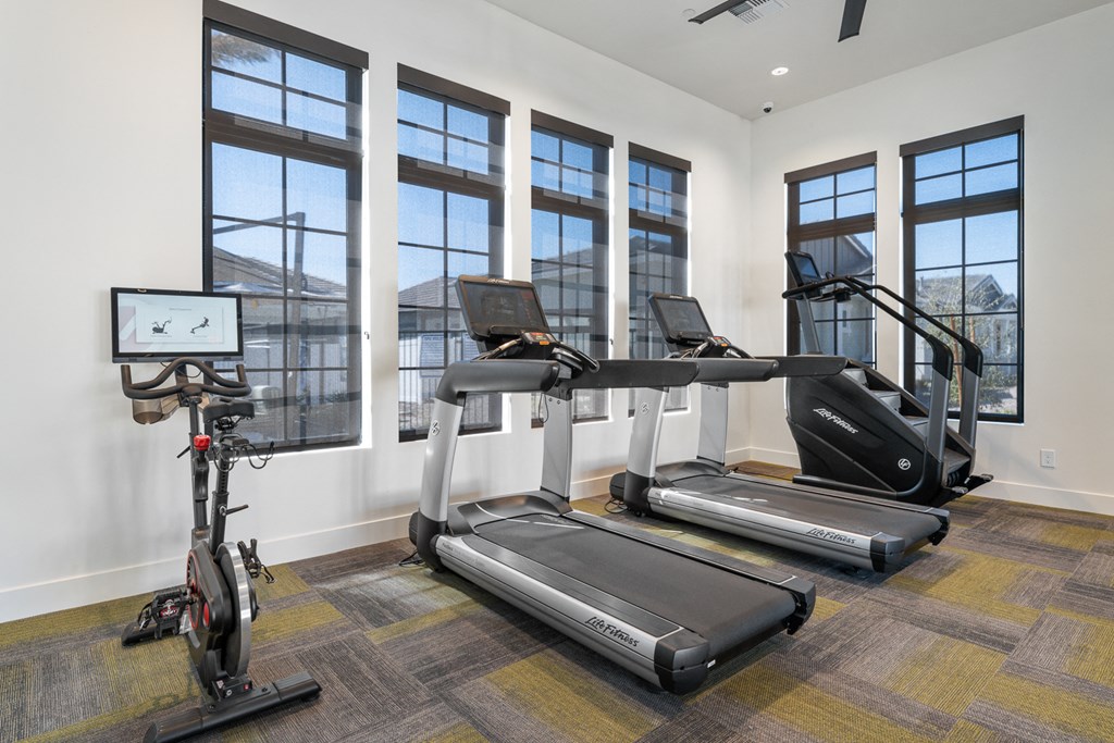 A treadmill, elliptical trainer and a stationary bike are in a room with a window.