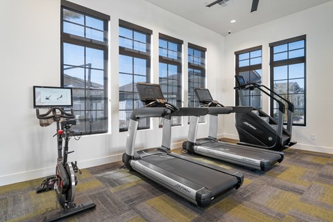 A treadmill, elliptical trainer and a stationary bike are in a room with a window.