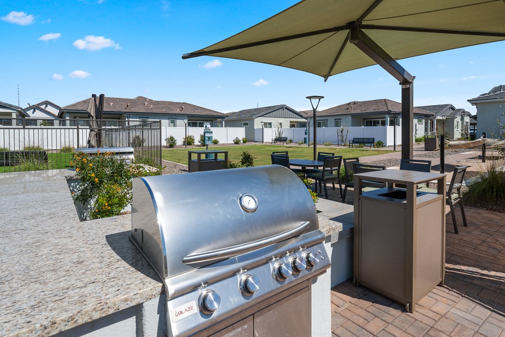 A silver gas grill is on a patio with a yellow umbrella above it.