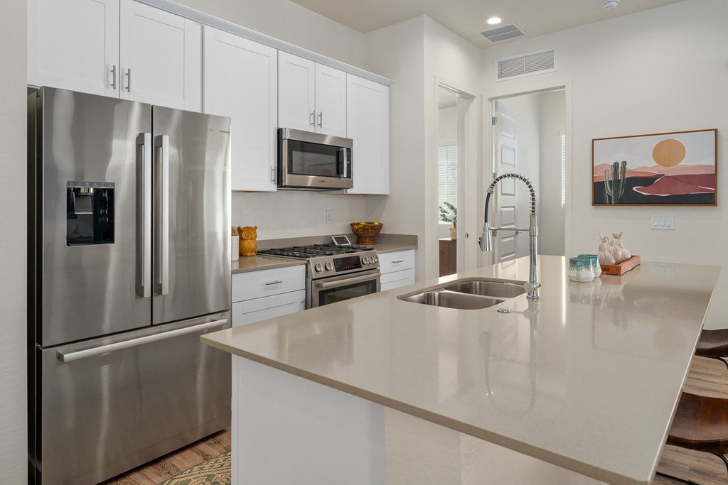 A modern kitchen with a stainless steel refrigerator, microwave, and white cabinets.
