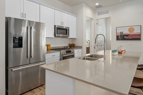 A modern kitchen with a stainless steel refrigerator, microwave, and white cabinets.