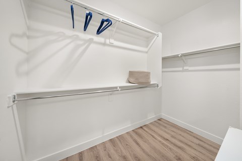 A white closet with clothes hanging on a rod.