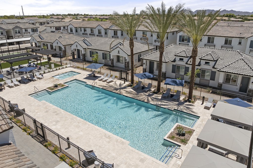 A swimming pool surrounded by palm trees and lounge chairs in a residential area.