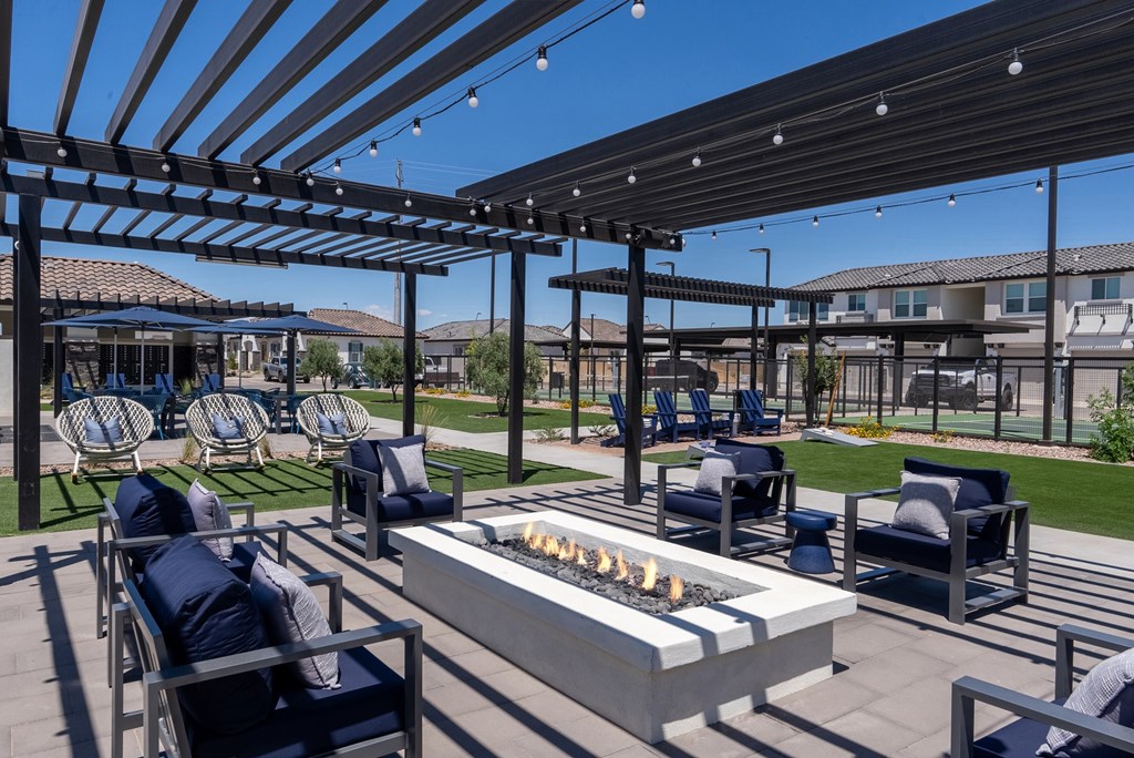 A patio with a fire pit and chairs under a pergola.