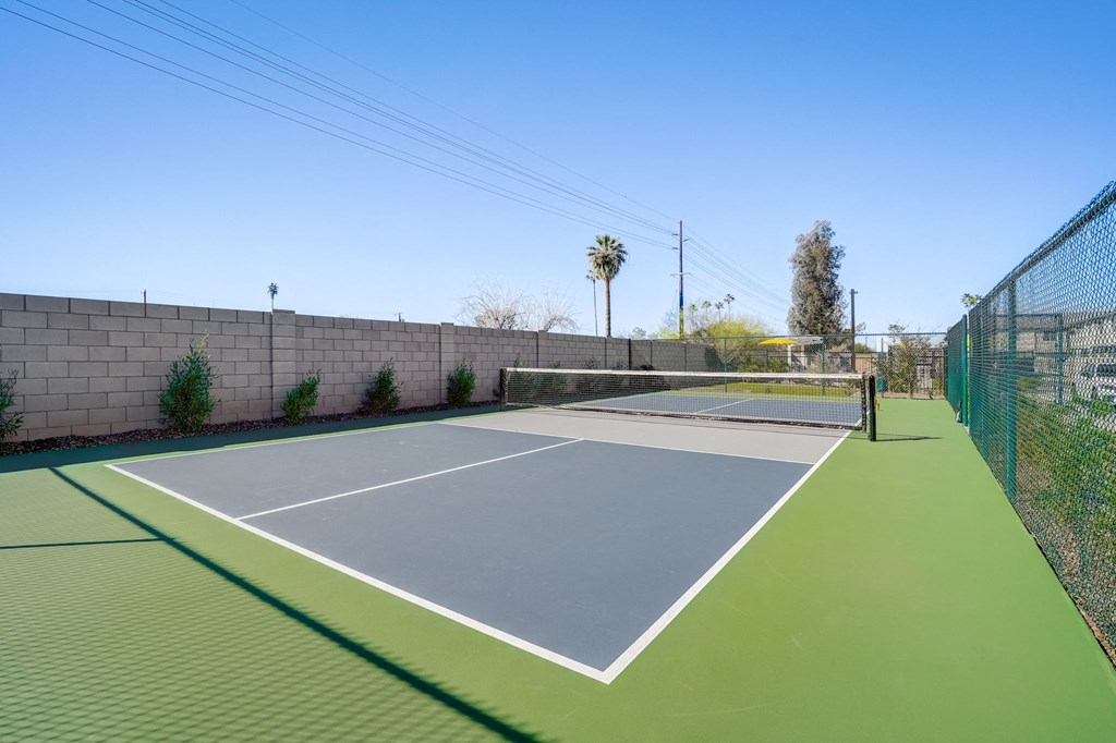 a tennis court with green turf and a fence on a sunny day