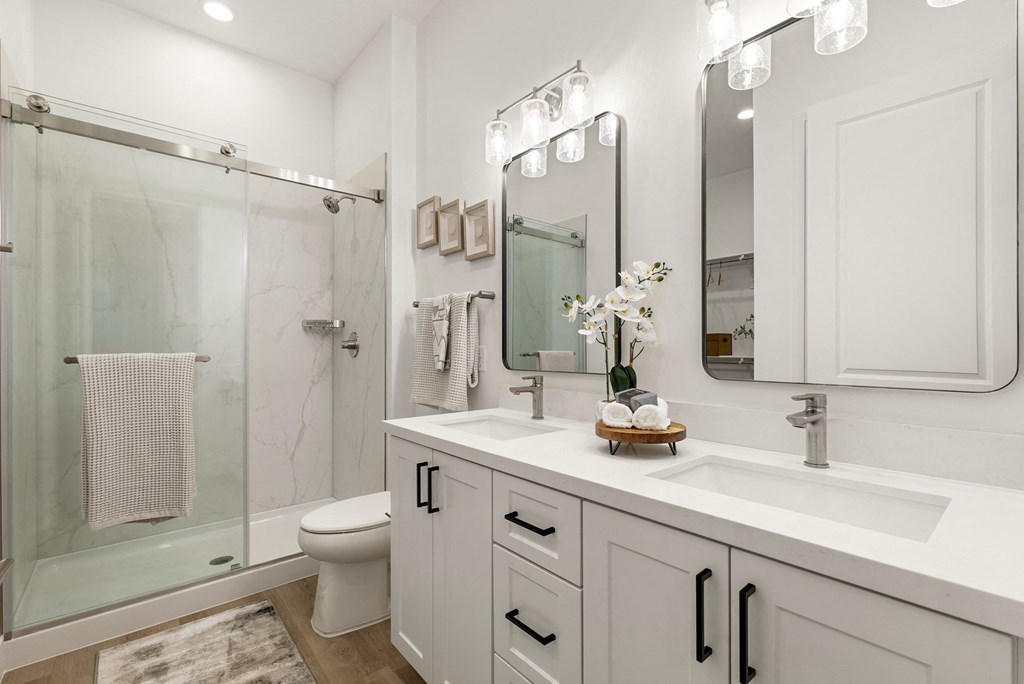 A white bathroom with a glass shower stall and a towel hanging on the glass door.