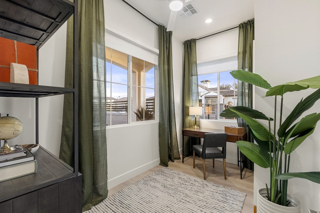 A room with a desk, chair, and a large window with green curtains.