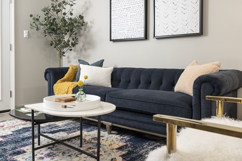 A living room with a blue couch, a white coffee table, and two framed pictures on the wall.