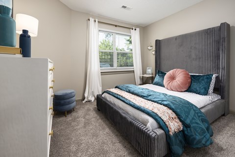 A bedroom with a large bed and a window with white curtains.