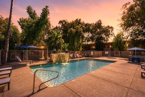 A pool surrounded by trees and chairs with a sunset in the background.