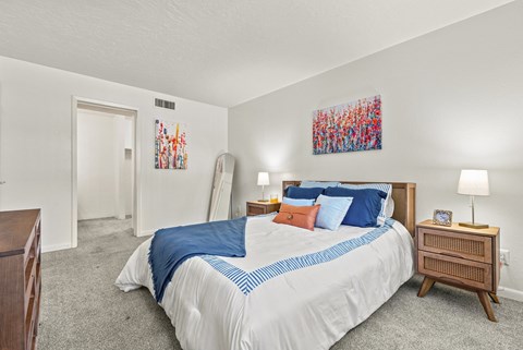 A bedroom with a bed, nightstand, and two paintings on the wall.