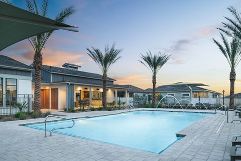 A swimming pool surrounded by palm trees and a building in the background.