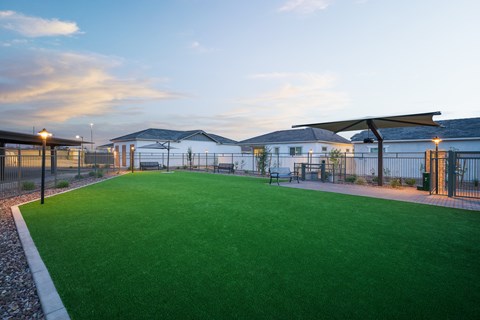 A green lawn in front of a building with a fence and bench.