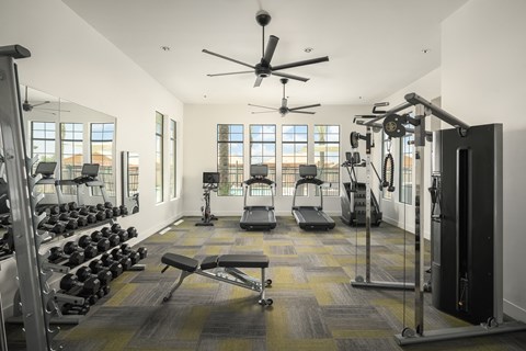 A spacious gym with a variety of equipment and a ceiling fan.