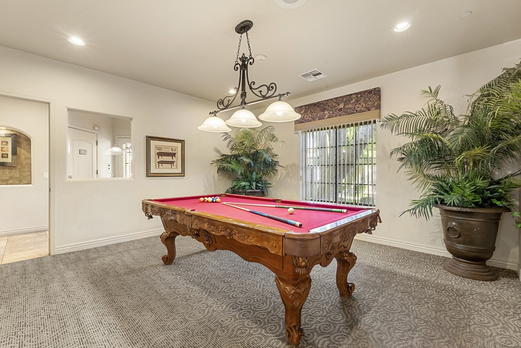 A pool table in a room with a chandelier and potted plants.