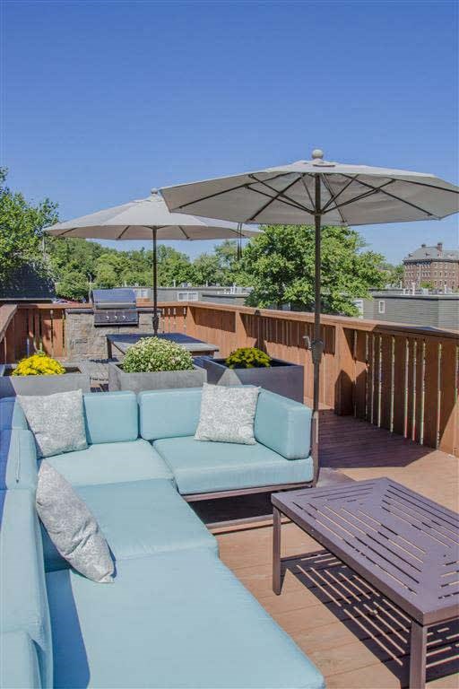 A blue couch is on a wooden deck with a white umbrella above it.