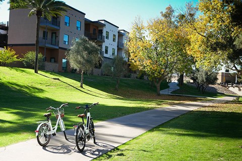 Two bicycles are parked on a path in front of apartment buildings.
