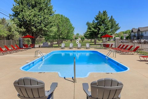 A large blue swimming pool surrounded by red chairs and umbrellas.