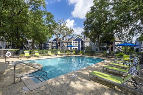 A pool surrounded by trees and chairs.