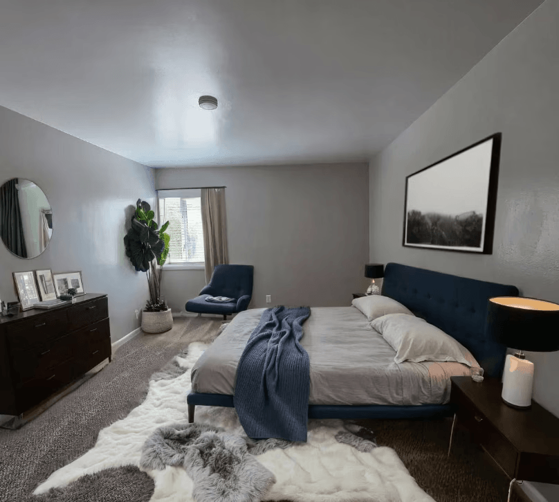 A bedroom with a bed, chair, and a mirror on the wall.