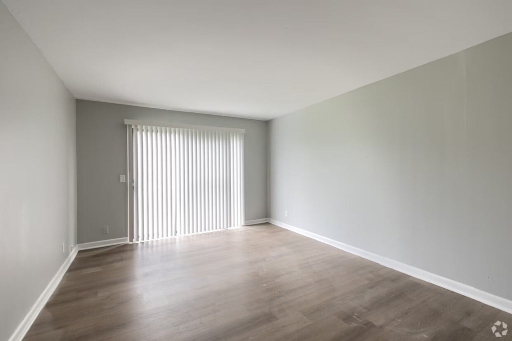 A room with wooden flooring and a window with blinds.
