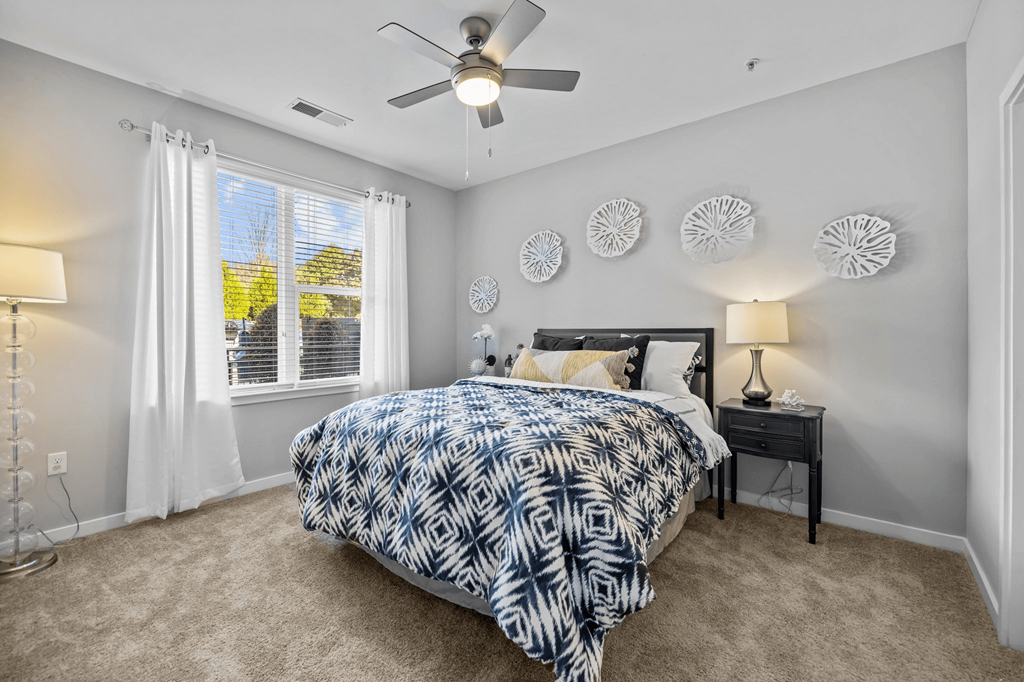 A bedroom with a patterned bedspread and a ceiling fan.