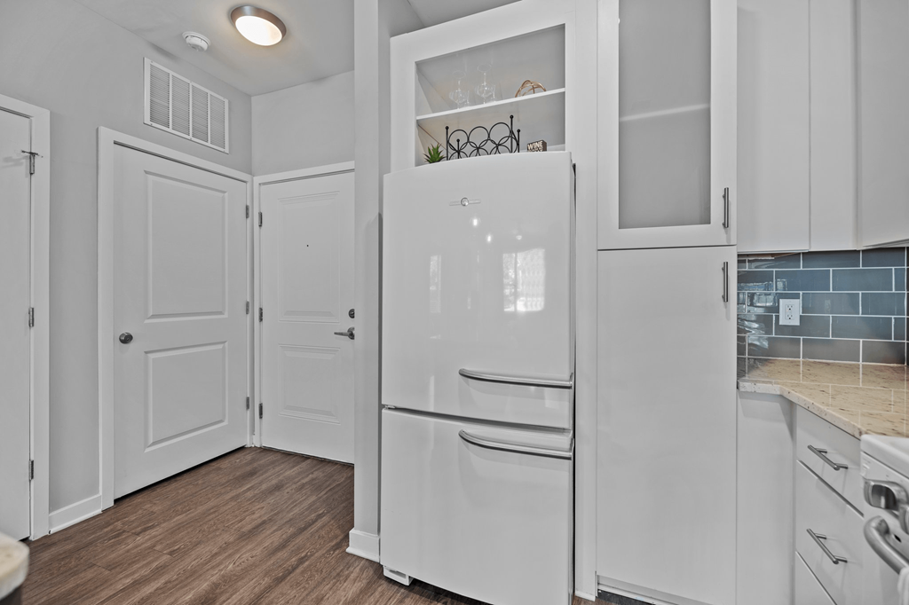 A white kitchen with a refrigerator, cabinets, and a wooden floor.
