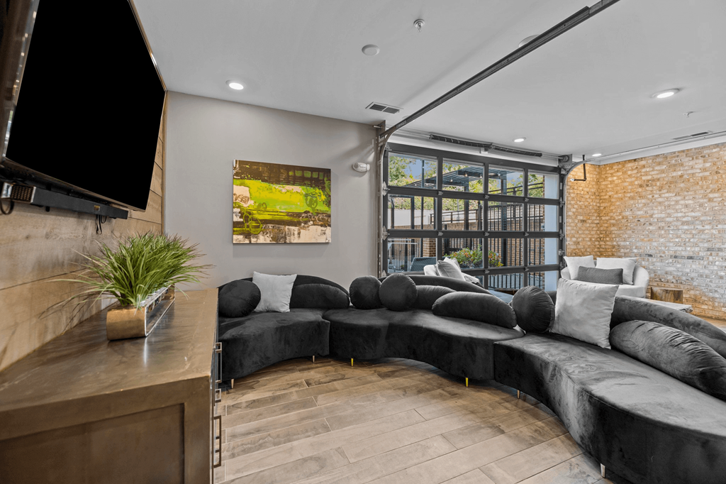 A modern living room with a large black sofa and a flat screen TV mounted on the wall.