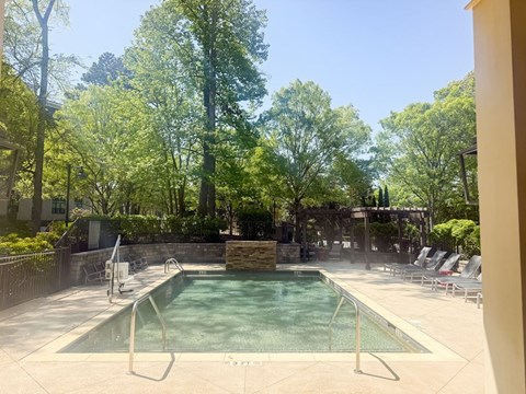 A pool surrounded by trees and chairs.