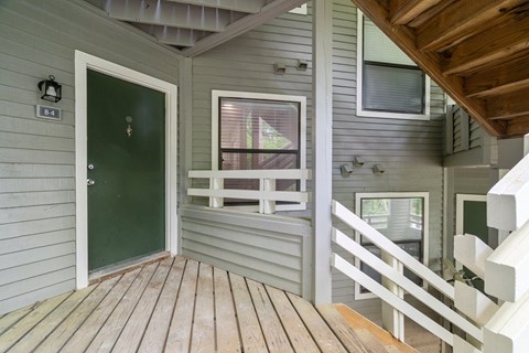 A green door is on the left side of a house with a white railing.