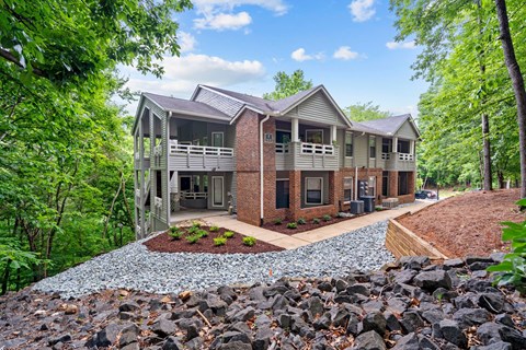 A house with a grey roof and a red brick chimney is surrounded by green trees.