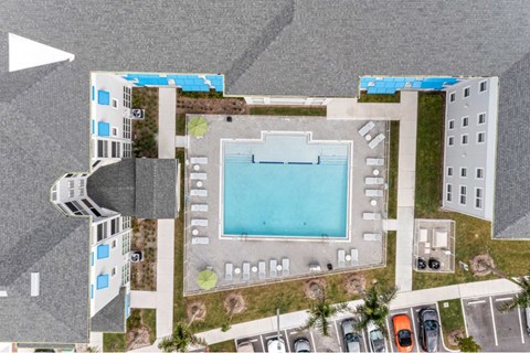 A large swimming pool is surrounded by a grassy area and a parking lot.