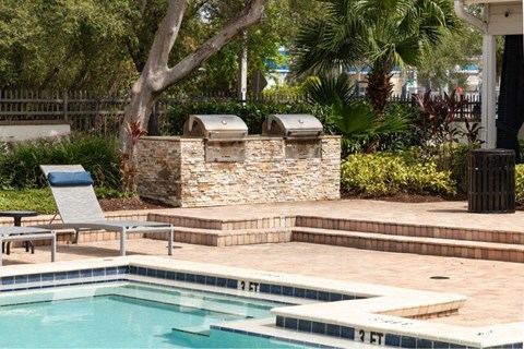 A pool with a stone wall and a grill next to it.