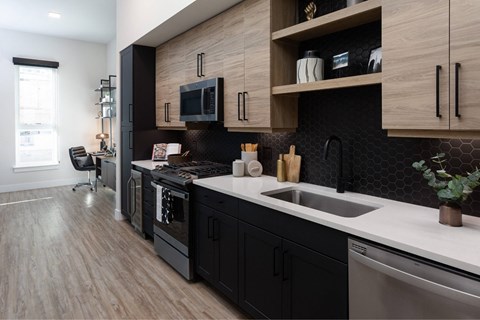 A modern kitchen with black cabinets and a wooden accent wall.