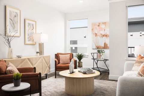 A living room with a brown sofa, a white armchair, a wooden coffee table, and a painting on the wall.