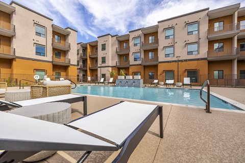 A pool surrounded by apartment buildings and lounge chairs.