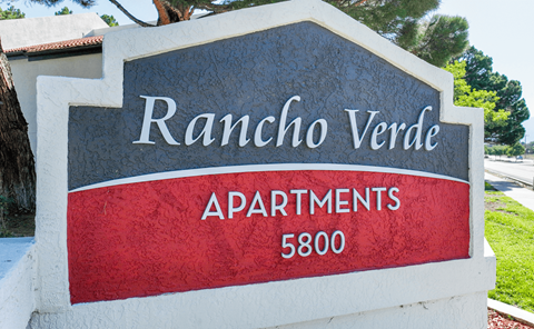 A sign for Rancho Verde Apartments stands in front of a tree.