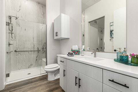 A bathroom with a marble shower and white cabinetry.