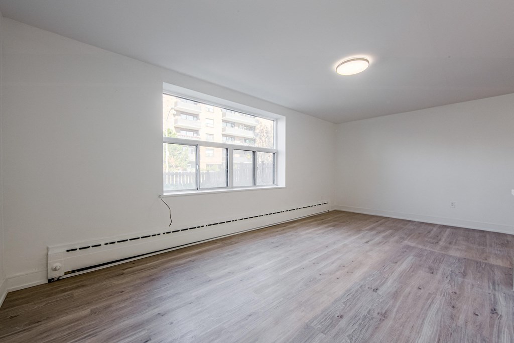 the living room of an empty apartment with wood flooring and a large window at 111 Cosburn, East York Ontario