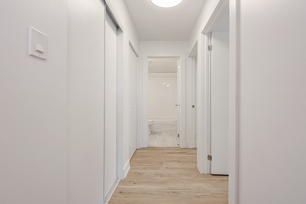 a corridor with white walls and wood floors and a white toilet at 111 Cosburn, East York, M4J 2L1